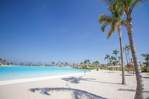 Ein Strand mit klarem, blauem Wasser, weißem Sand und Palmen.