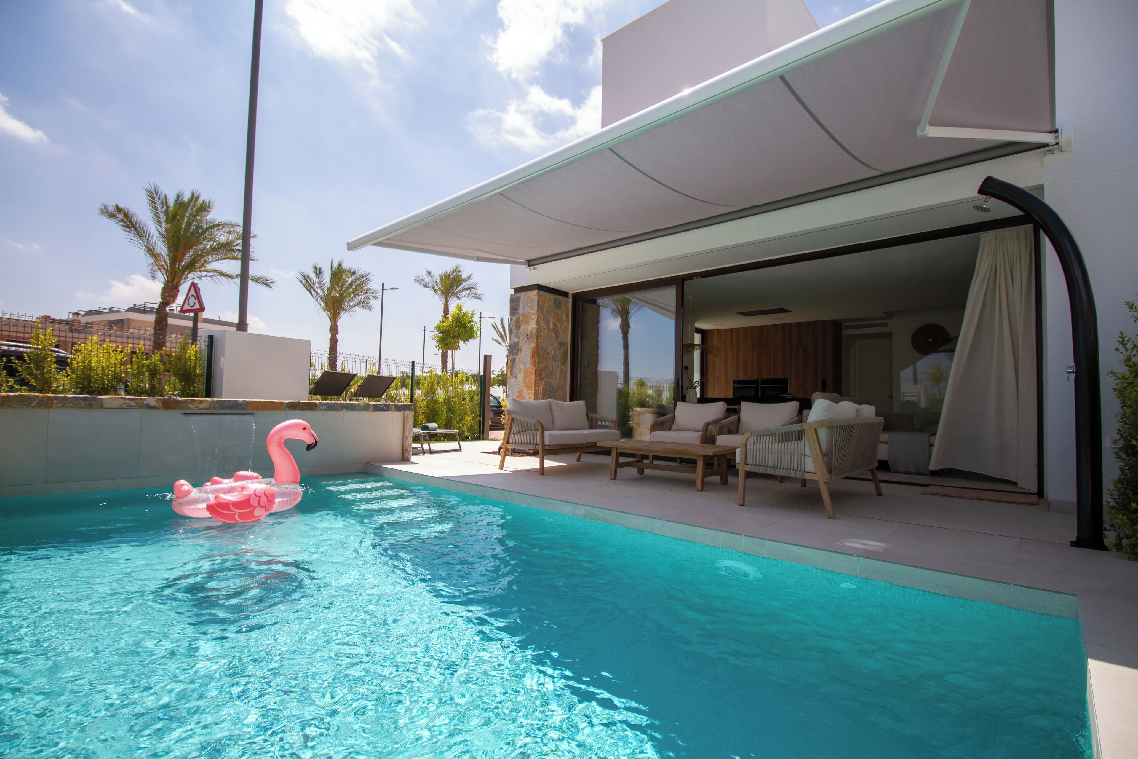 A swimming pool with a pink flamingo float, outdoor furniture, and a modern house with a covered patio.