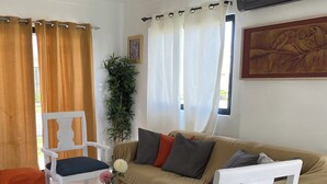 Una sala de estar con un sofá color beige, sillones blancos, una mesita pequeña con un florero y cojines naranjas.
