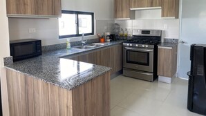 Cocina moderna con armarios de madera, encimera de granito, electrodomésticos de acero inoxidable y un ventanal que proporciona luz natural.