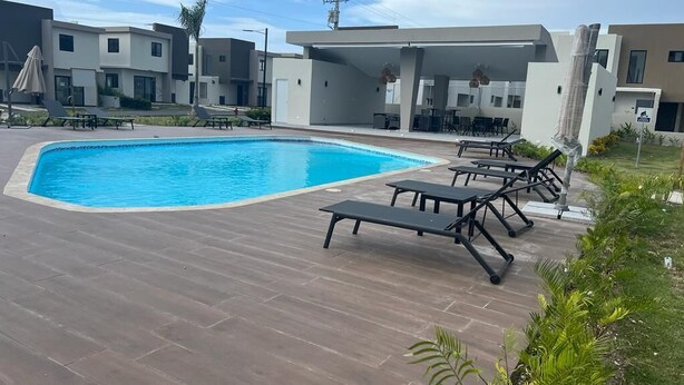 Una piscina con sillones de descanso y una zona cubierta, rodeada de edificios modernos.