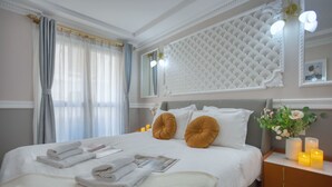 Una cama bien tendida con sábanas blancas y dos almohadas color mostaza, una mesita de noche con velas y un panel decorativo en la pared.