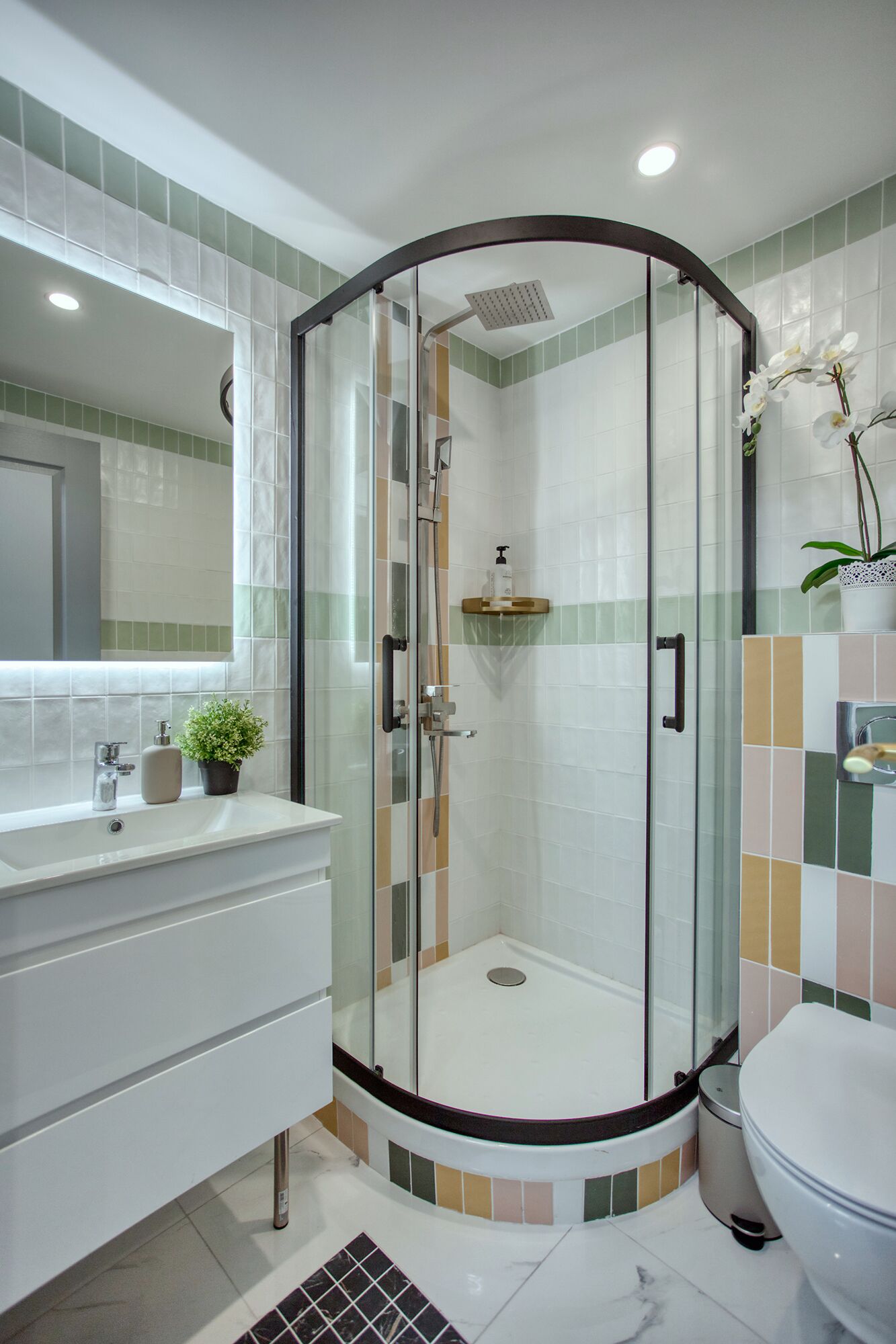 Ein modernes Badezimmer mit einer gläsernen Dusche, einem weißen Waschbecken mit Pflanze und einer Toilette.