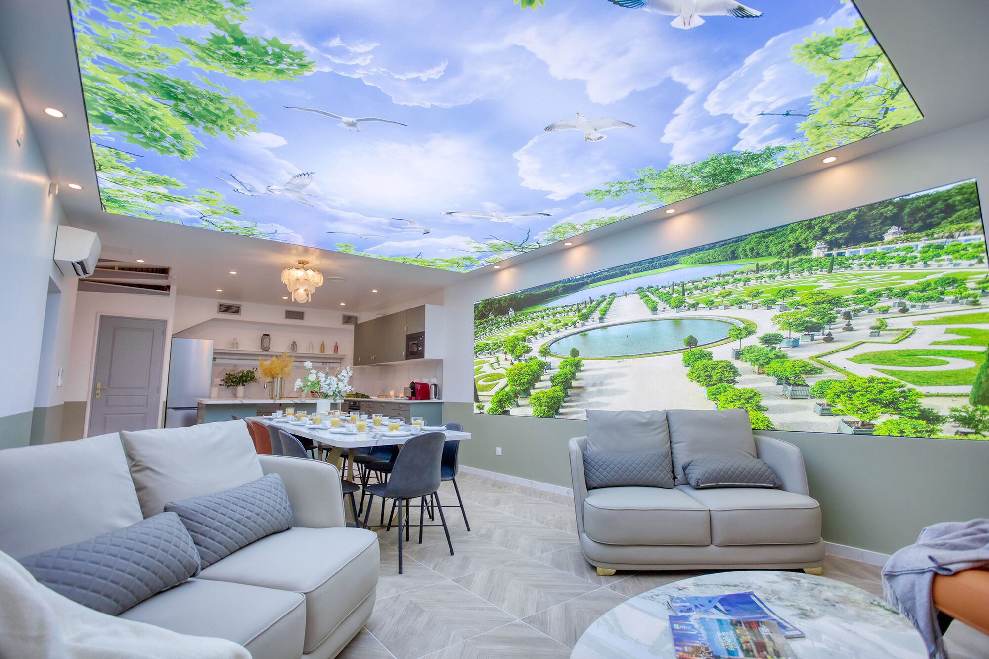 A modern room with a large digital ceiling display, a dining area, and a seating area with a view of a landscaped garden.