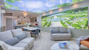 Una sala de estar moderna con comedor, un sofá, una mesa de centro y un gran mural de un jardín y fuente de agua.