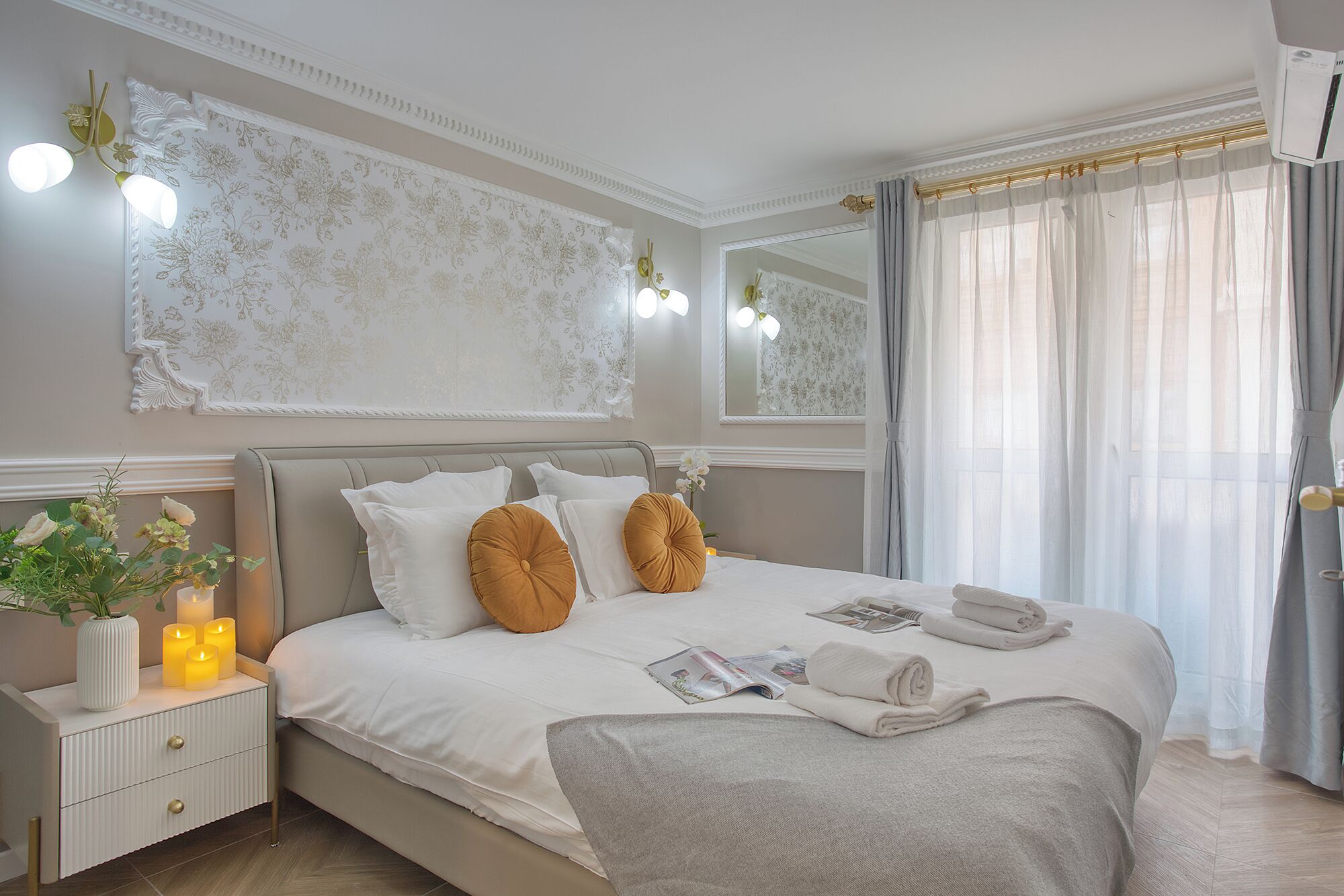 Une chambre bien rangée, avec un lit, des tables de chevet, un miroir et une fenêtre avec des rideaux.