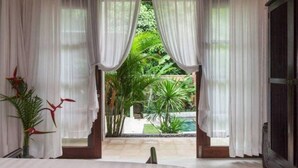 A bedroom with a large bed, white curtains, and a view of a garden and pool. - 2 BR Tranquil Villa 10 Min Walk to Seminyak Beach (Kuta Utara)