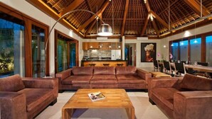Un amplio salón con techo de madera, sofás de cuero, una mesa de centro de madera y una cocina al fondo.