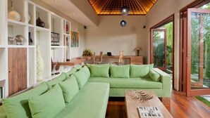 Una sala de estar moderna con un sofá seccional verde, piso de madera, un techo con diseño de celosía de madera y un ventanal que da a un área exterior.