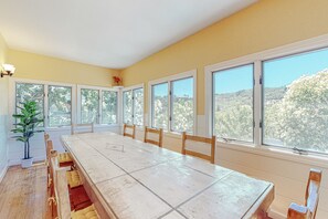 Enjoy meals with a view in this dining area, featuring a long table and large windows overlooking the surrounding landscape.