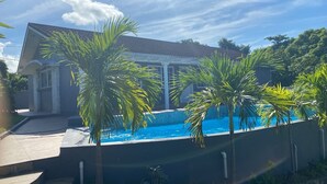 Um imóvel residencial com piscina, palmeiras e uma casa com telhado telhado.