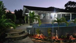 Uma casa moderna com piscina, cercada por palmeiras e um espaço de varanda bem iluminado.
