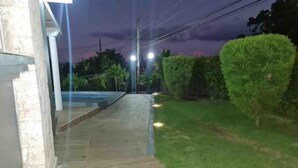 Um caminho leva a um edifício com piscina, cercado por grama bem cuidada e sebes.