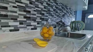 Uma cozinha com bancada de mármore, um pote de vidro com limões e um escorredor de louça com pratos.
