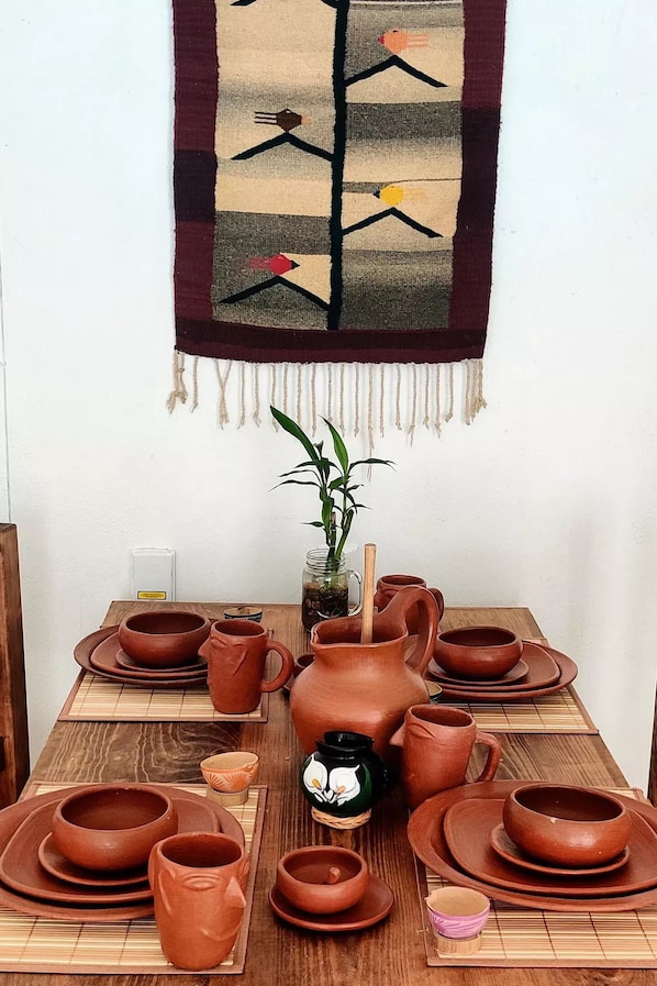 A table set with various clay pottery items, including cups, plates, and a pitcher, arranged on a wooden table with a bamboo placemat. - Plumeria house (Santa Cruz Xoxocotlán)