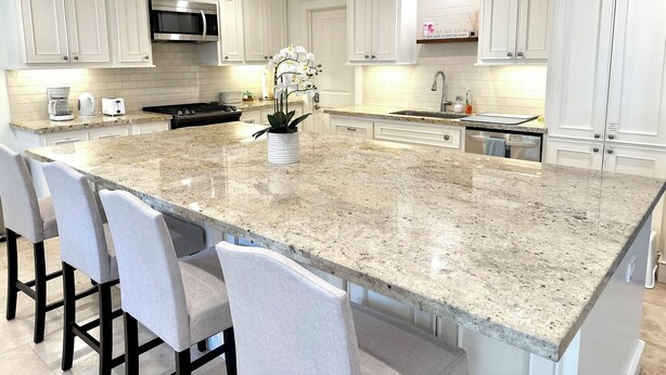Une cuisine moderne avec des meubles blancs, un îlot en granit, des tabourets de bar, des appareils en acier inoxydable et des luminaires suspendus.