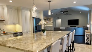 Une cuisine moderne avec des armoires blanches, un îlot en granit et des luminaires suspendus.