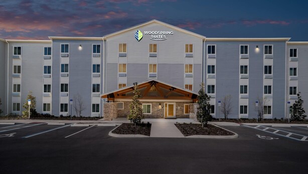 A multi-story hotel with a flat roof, a central entrance with a covered walkway, and a parking lot with marked spaces.