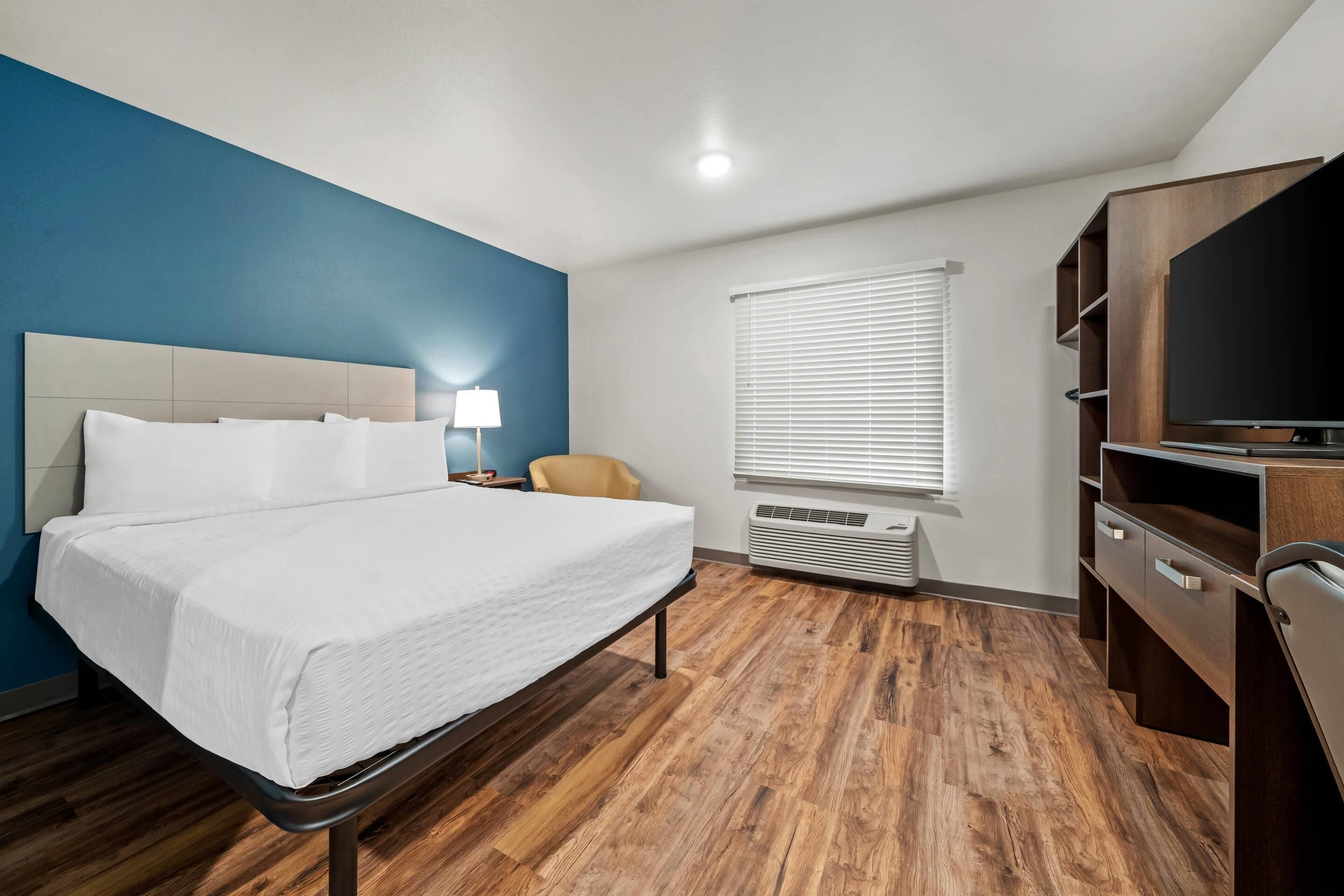 A hotel room with a bed, a desk, a chair, a TV, and a window with blinds.