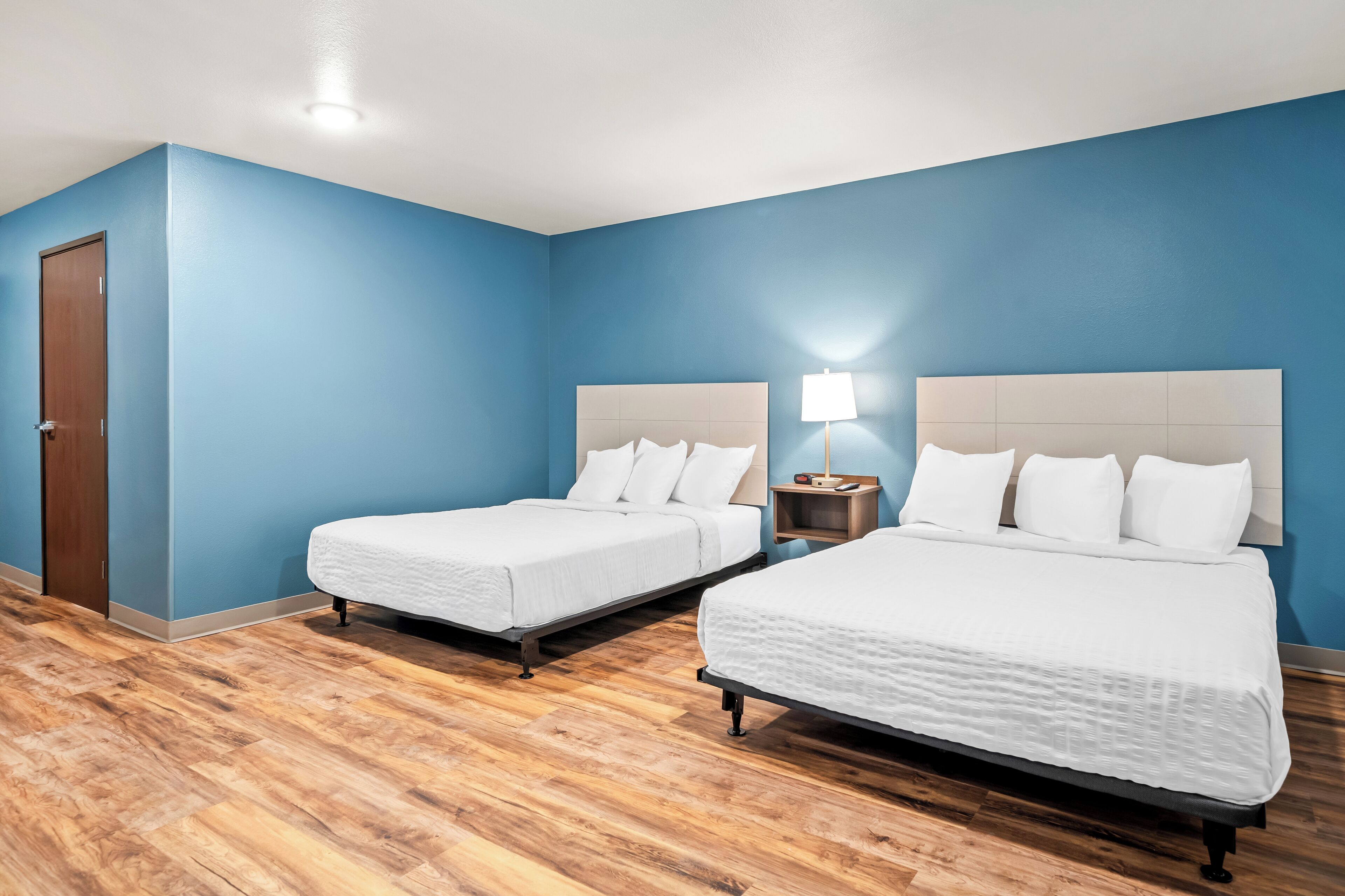 A hotel room with two beds, a wooden floor, and blue walls.