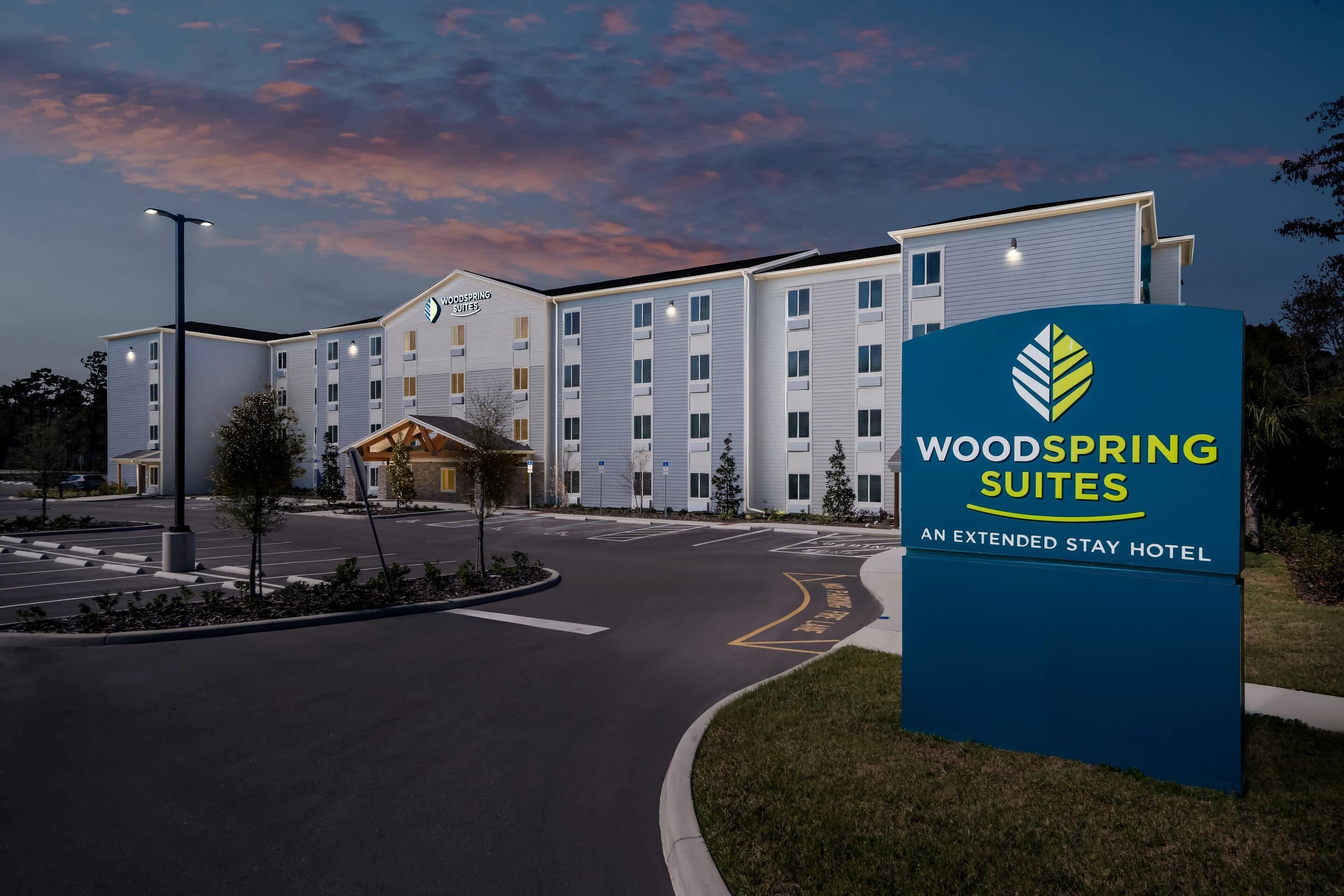 A hotel with a sign reading 'Woodspring Suites' and 'An Extended Stay Hotel.'