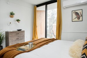 A bedroom with a bed, a dresser, a window with yellow curtains, a plant, and a wall-mounted picture of an owl.