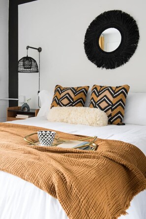 Un lit bien fait, avec une couverture marron, deux coussins à motifs, un coussin blanc et moelleux, et un élément de décoration murale noir de forme circulaire.