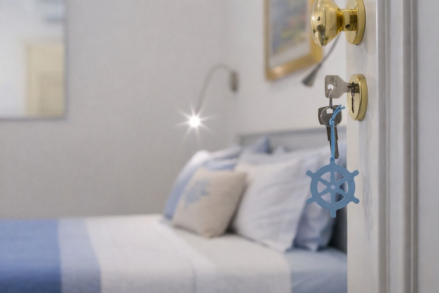 A bedroom with a bed, pillows, a nightstand, and a wall-mounted key holder with a ship's wheel decoration.