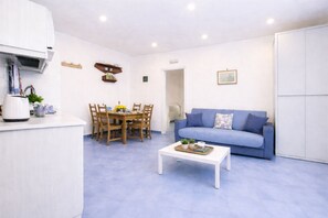 A modern living room with a blue sofa, a dining table with chairs, a coffee table, and a white cabinet.
