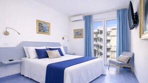 Hotellihuone, jossa on sänky, tuoli, televisio ja parveke, jossa on verhot.