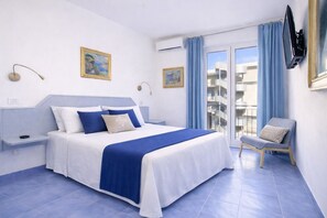 Una habitación de hotel con cama, una silla, un televisor y un balcón con cortinas.