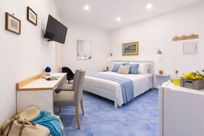 A bedroom with a bed, desk, chair, TV, and a small table with a bottle and lemons.