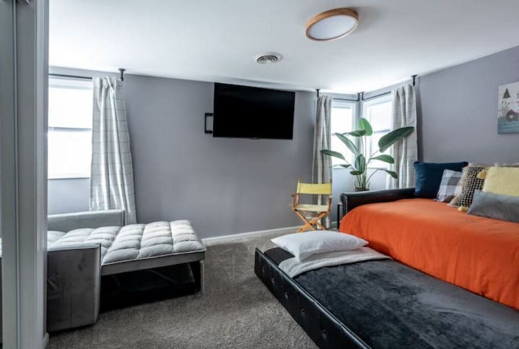 Una camera da letto con un letto, una panca, una TV e una finestra con tende.
