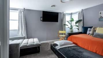 Una camera da letto con un letto, una panca, una TV e una finestra con tende.