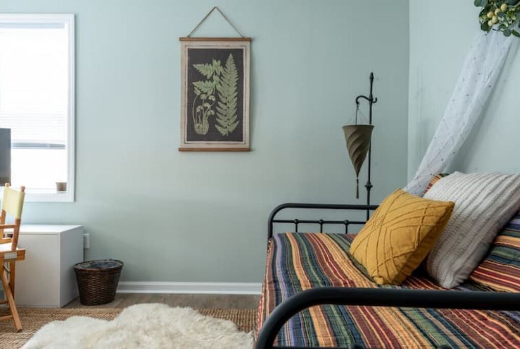Un dormitorio con una cama, una planta enmarcada, una lámpara y una ventana.