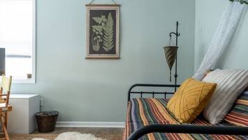 Un dormitorio con una cama, una planta enmarcada, una lámpara y una ventana.