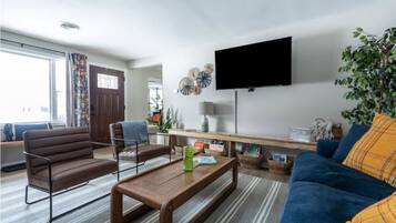 Una sala de estar con sofá, sillón, mesa de centro y televisor de pantalla plana montado en la pared.