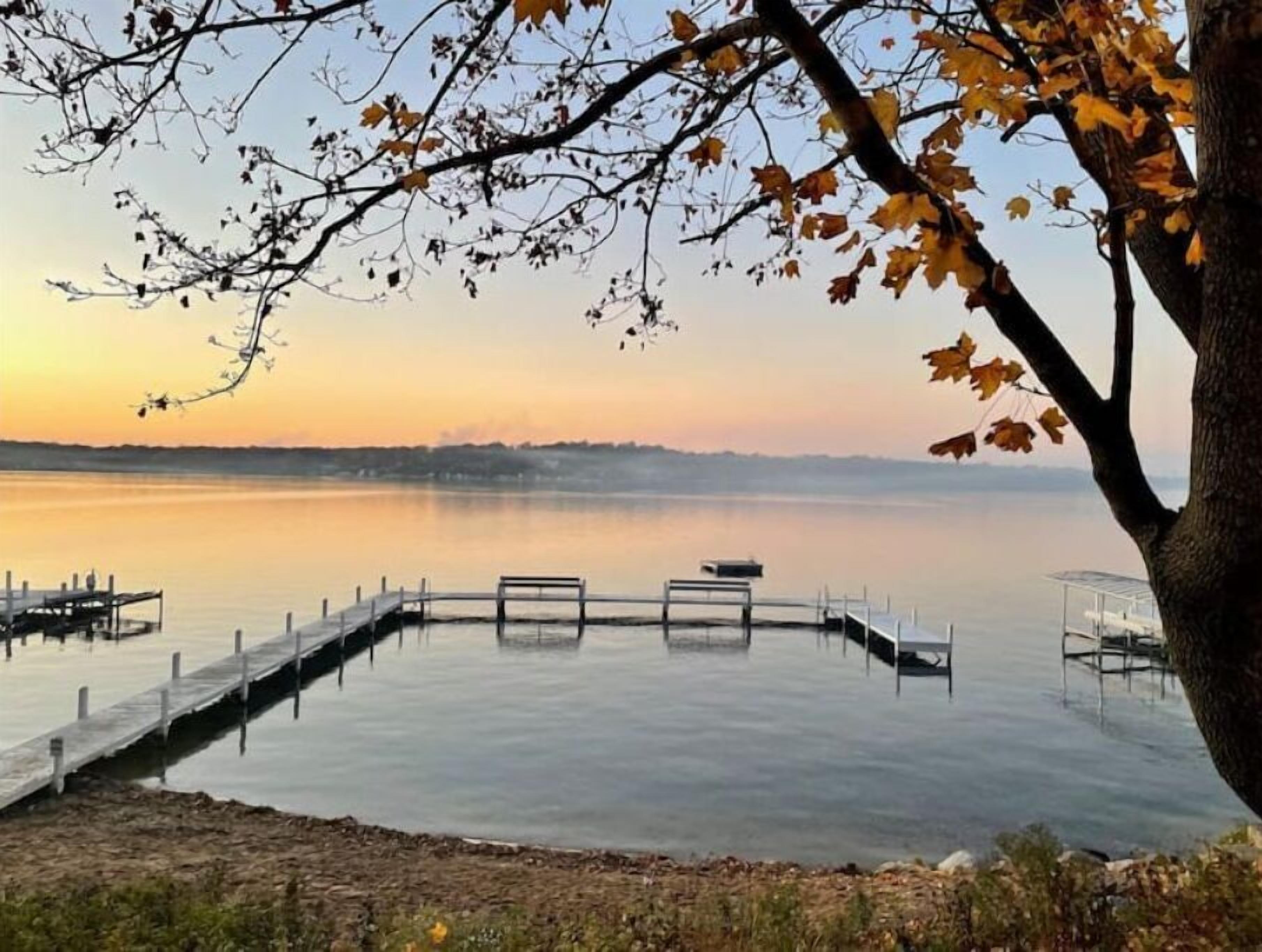 Un lac paisible, avec une jetée en bois qui s’avance sur l’eau, entouré d’arbres aux feuilles d’automne.