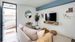 A modern living room with a sofa, a TV, a plant, and a dining area.