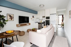 Uma sala de estar moderna com um sofá branco, uma televisão e um espaço de jantar com uma mesa e cadeiras de madeira.