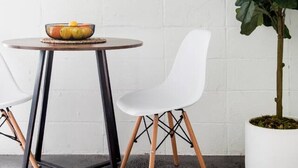 A modern dining area with a round table, white chairs, a large mirror, and a potted plant.