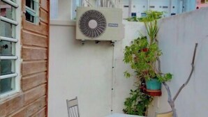 A small outdoor patio with a table and chairs, a potted plant, and a wall-mounted air conditioning unit. - Studio Lumineux Dans Quartier Calme, Avec Terrasse, 5 mn à Pied du Centre Ville (Basse-Terre)