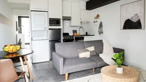 Un espacio habitable compacto con kitchenette, sofá gris y un pequeño comedor.