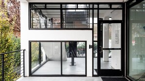 Una entrada de edificio moderna con puerta de vidrio, baranda metálica y vista de una escalera que conduce a un nivel superior.
