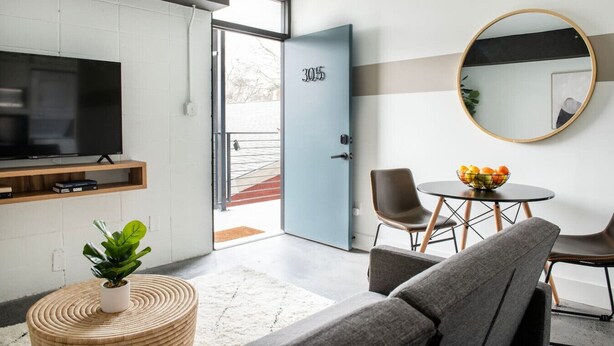 Una sala de estar moderna con televisor, asientos, una mesa de comedor con fruta y una puerta con el número 305.
