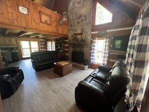 Ein rustikales Blockhaus-Interieur mit Kamin aus Stein, schwarzen Ledersofas, einem Holztisch und einem Fernseher.