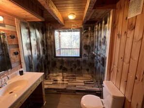 Ein rustikales Badezimmer aus Holz mit großem Fenster, einem Waschbecken und einer Toilette.