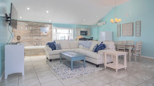A modern living room with a beige sofa, a coffee table, and a dining area with a table and chairs. - Elegant Suite with Jacuzzi (Hancock)