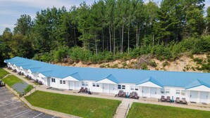 A row of white cabins with blue roofs, arranged in a linear fashion along a parking lot, surrounded by a forested area. - Elegant Suite with Jacuzzi (Hancock)