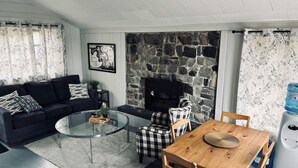 Una sala de estar con sofá, una mesa de centro de vidrio, chimenea, mesa de comedor con sillas y dispensador de agua.